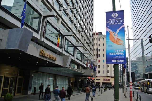 Плакат Shen Yun Performing Arts, розміщений перед готелем Sheraton у столиці Бельгії Брюсселі. Лідер Комуністичної партії Китаю Сі Цзіньпін запланував зупинитися у цьому готелі, і китайське консульство поставило вимогу прибрати ці плакати.